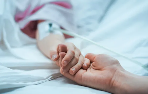 Foto de una mano de una persona en la cama de un hospital agarrada por otra mano más joven