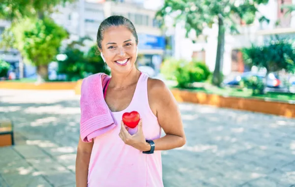 Foto de una mujer adulta con ropa deportiva que sonríe a cámara mientras sostiene un corazón de espuma