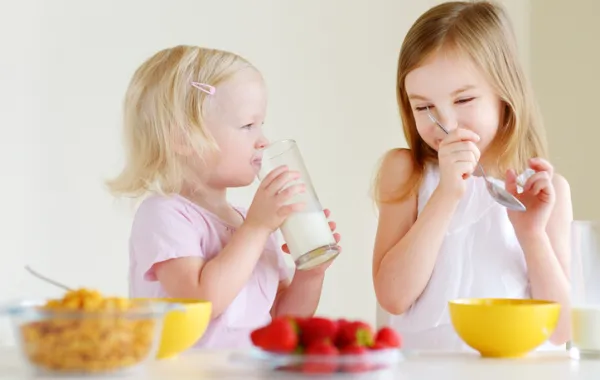 Foto de dos niños desayunando fruta, leche y cereales