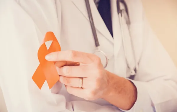 Foto de un médico que sostiene en la mano un lazo naranja símbolo de esclerosis multiple