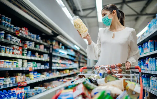 Foto de una mujer en un supermercado con un carro de comida y leyendo la etiqueta de un producto