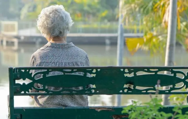 Mujer mayor sentada en un banco mirando a un lago