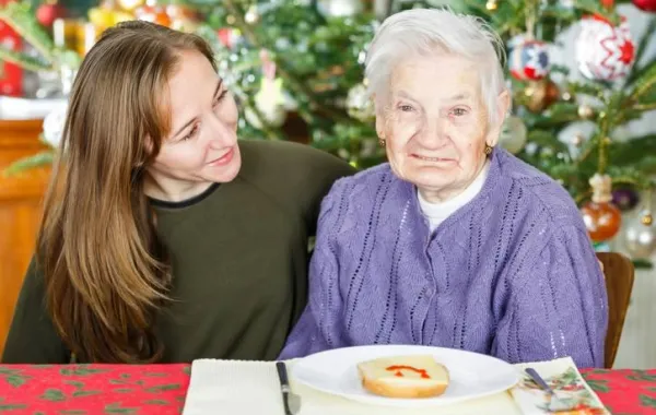 Una mujer joven acompañando a una mujer mayor sonriendo a cámara en una comida navideña
