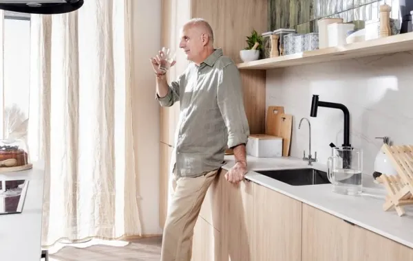 Hombre mayor bebiendo un vaso de agua en una cocina moderna bien equipada