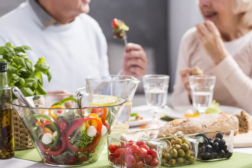 Foto de dos personas adultas sentadas en una mesa con alimentos saludables