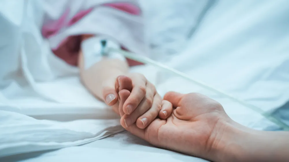 Foto de una mano de una persona en la cama de un hospital agarrada por otra mano más joven