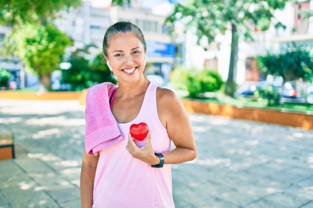 Foto de una mujer adulta con ropa deportiva que sonríe a cámara mientras sostiene un corazón de espuma