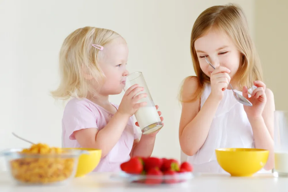 Foto de dos niños desayunando fruta, leche y cereales