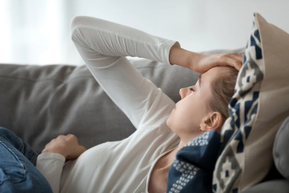Foto de una mujer joven tumbada en un sofá y con la mano en la cabeza por el dolor