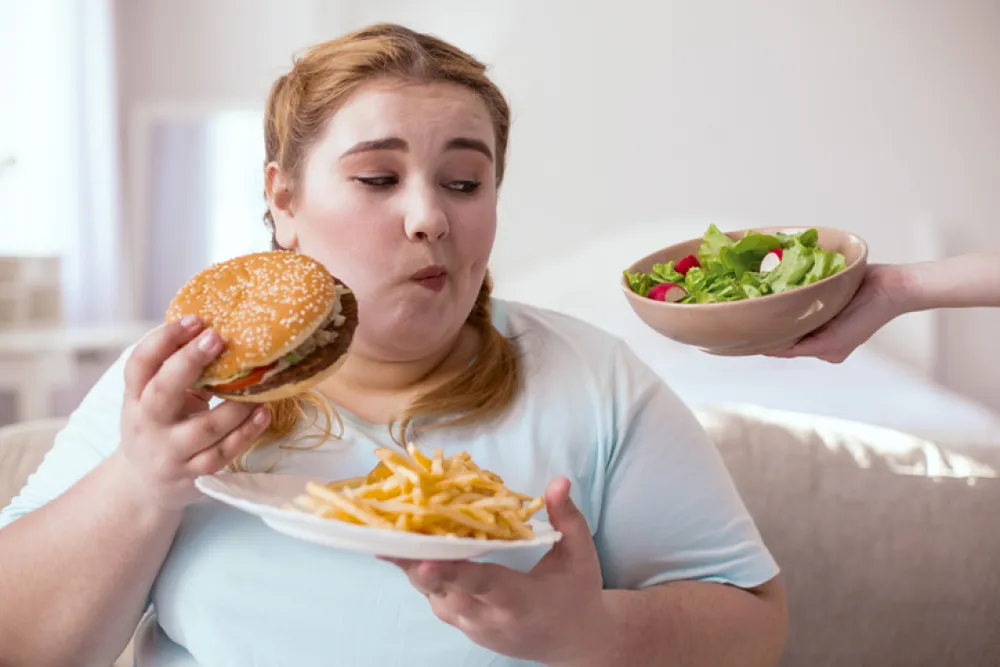 Foto de una chica joven con sobrepeso comiendo comida no saludable