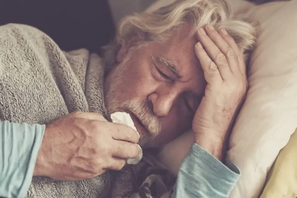 Hombre mayor abrigado en la cama con un pañuelo. Gripe A.
