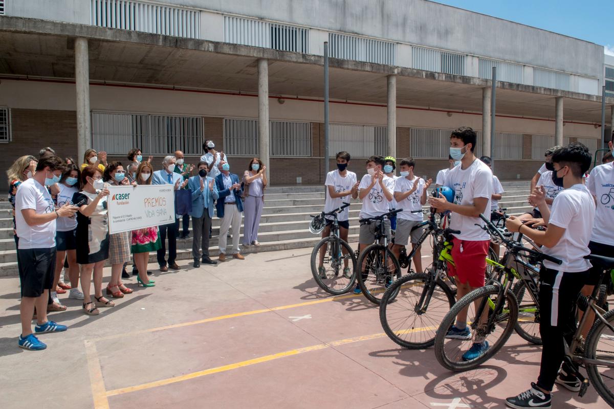 Fotografía de profesores y alumnos sujetando un cheque y jóvenes montando en bici