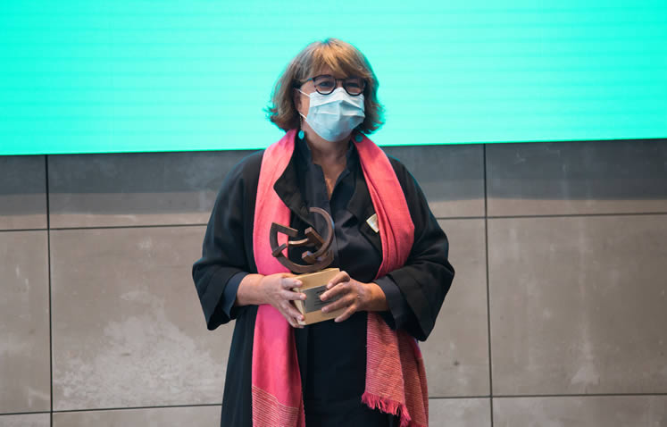 Fotografía de mujer con mascarilla sosteniendo un trofeo