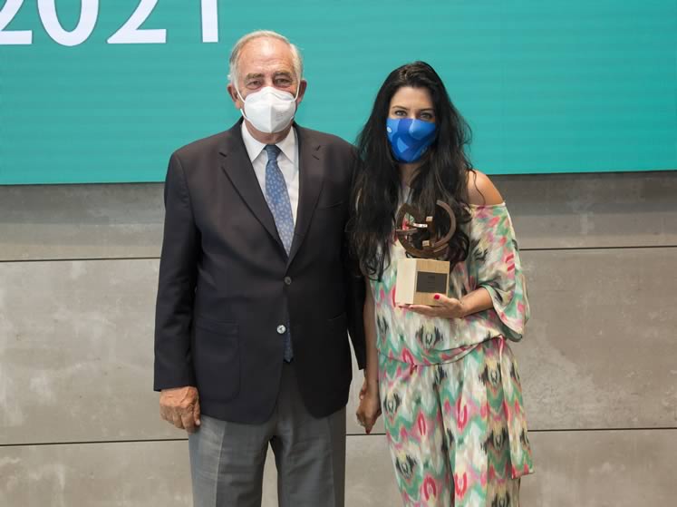 Fotografía de mujer con mascarilla sosteniendo un trofeo junto a un compañero