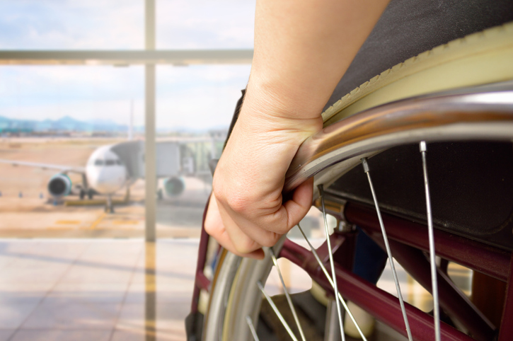 Foto de una persona en silla de ruedas que mira por la venta de un aeropuerto con un avión de fondo