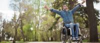 Foto en un parque de un chico en silla de ruedas con los brazo abiertos celebrando