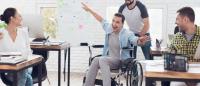 Foto de un grupo de personas en una clase  mirando a un chico con silla de ruedas que está riendo