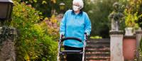 Foto de una mujer mayor andando por un jardin con un andador