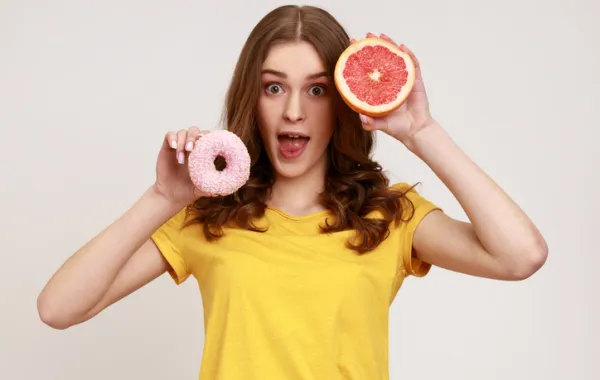 Foto de uma mujer que sostiene en una mano un donuts y en la otra un pomelo