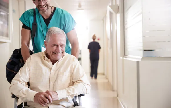 Foto de un señor mayor en silla de ruedas empujado por un enfermero