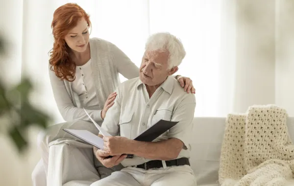 Foto de un señor mayor que está leyendo acompañado de un mujer joven