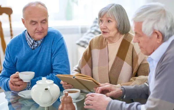 Foto de tres personas mayores bebiendo un te y leyendo un libro los tres juntos