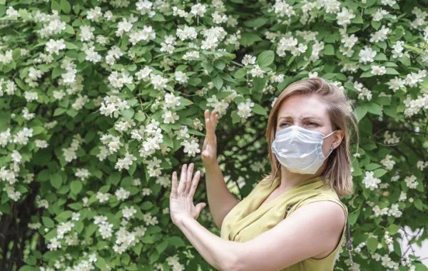 Foto de una mujer con mascarilla al lado de una arboleda con flores