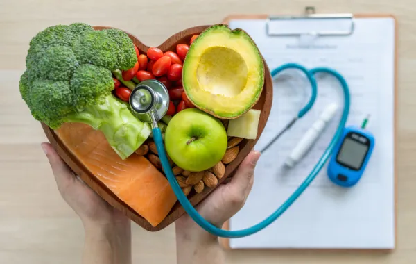 Foto de un corazon en madera lleno de frutas y verduras al lado de un medidor de glucosa