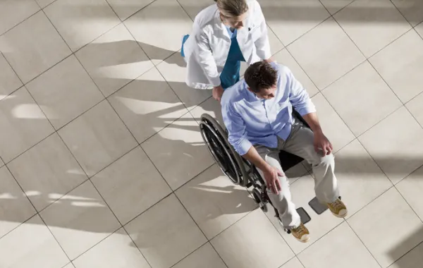 Foto de un señor en silla de ruedas acompañado por una enfermera