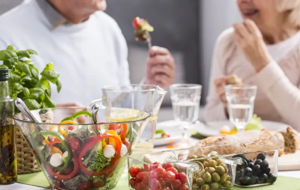 Foto de dos personas adultas sentadas en una mesa con alimentos saludables