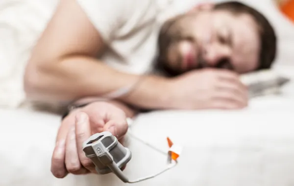 Foto de un hombre que duerme en la cama con un controlador de pulos en el dedo