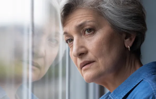 Foto de una señora adulta mirando por la ventana con cara triste