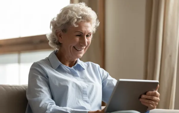 Foto de una señora mayor sonriendo mientras lee en una tablet