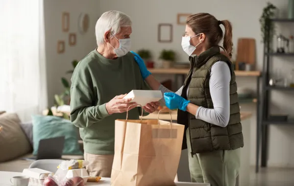 Foto de un señor mayor que recibe una bolsa con comida de una chica joven