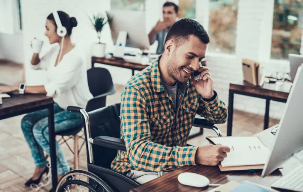 Foto de un chico joven en silla de ruedas atendiendo un teléfono en una oficina