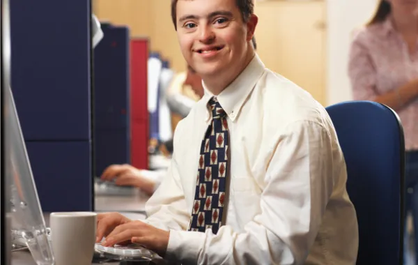Foto de un joven con síndrome de down vestido con corbata y delante de un ordenador