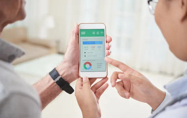 Foto de una personas enseñándole a otra la pantalla del móvil con el gesto de explicarle la información que se ve