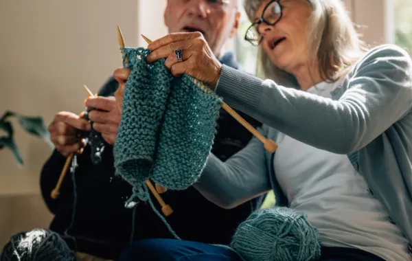 Foto de una señora mayor enseñando a tejer a otro señor mayor