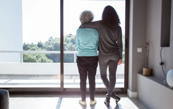 Foto de una mujer mayor y una mujer joven de que miran juntas por la ventana de un piso