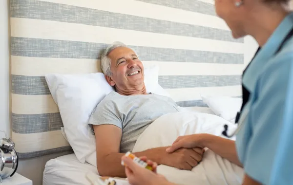 Foto de un señor mayor tumbado en su cama y con atendido por una doctora