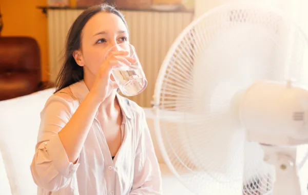 Foto de una mujer bebiendo agua frente a un ventilador