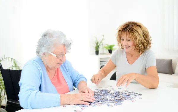 Foto de una señora mayor acompañada por una señora más joven haciendo un puzzle juntas