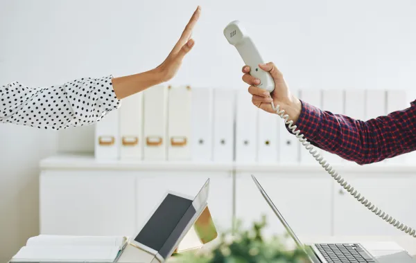 Foto de la mano de una personas con un teléfono que se lo pasa a otra persona que no quiere coger la llamada