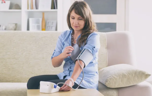 Foto de una mujer tomandose la tension en casa con un aparato de tension