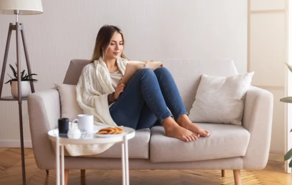 Foto de una mujer joven sentada en un sillón mientras lee un libro