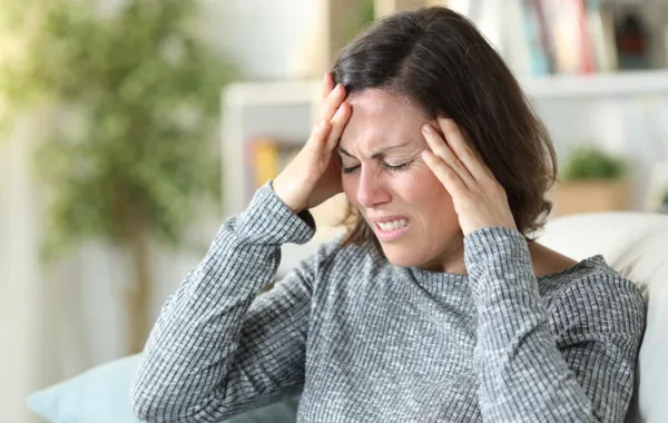 Foto de una mujer con las manos en la cabeza y con gesto de dolor