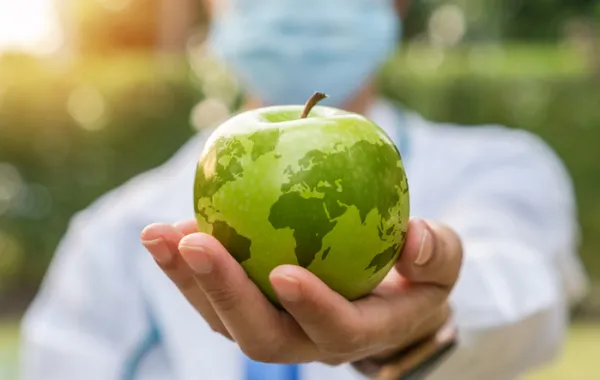 Foto de una persona sosteniendo una manzana con el dibujo del mundo impreso en la superficie de la manzana
