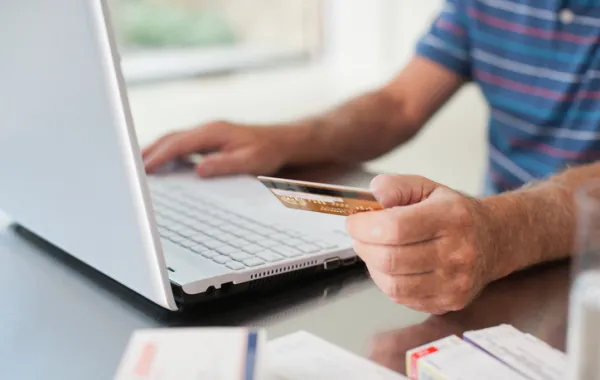 Foto de una persona delante de un ordenador realizando una compra online y sosteniendo una tarjeta de crédito en la mano