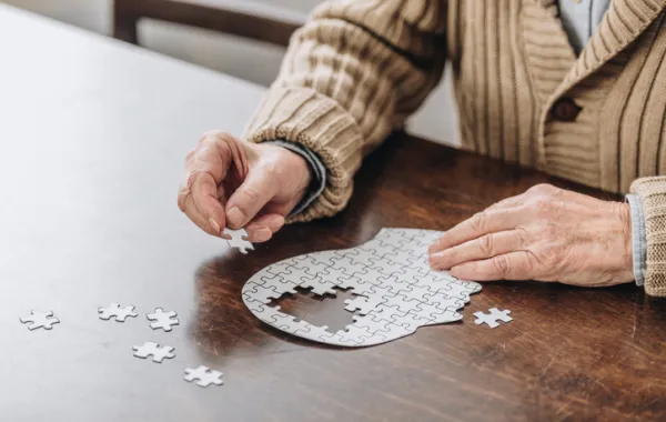 Foto de unas manos de persona mayor haciendo un puzle con forma de cabeza