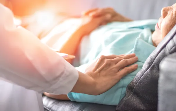 Foto de una mano que se apoya en una persona tumbada en una cama y enferma